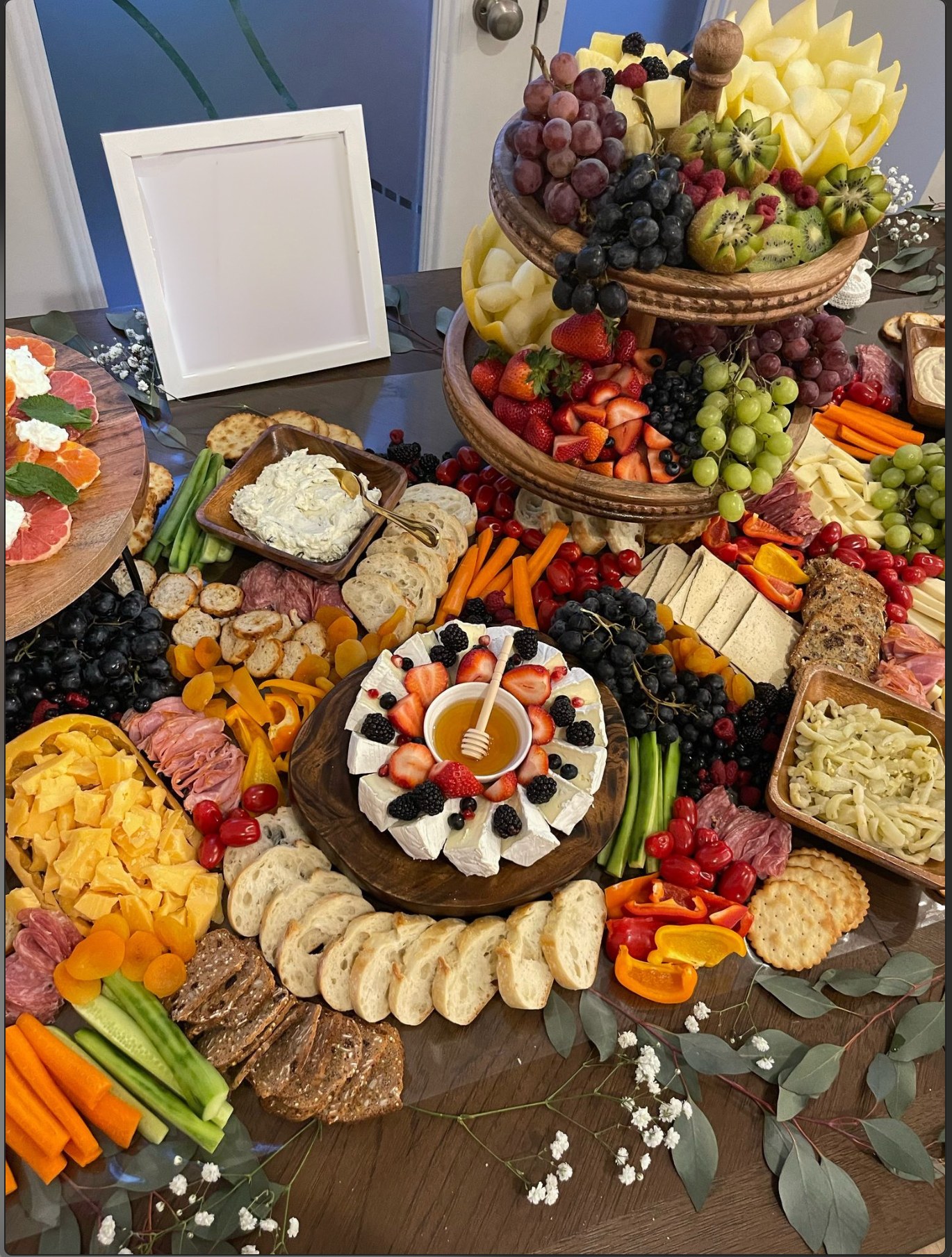Luxurious grazing table with tiered fruit display, brie with berries and honey, and abundant charcuterie spread with eucalyptus garnish